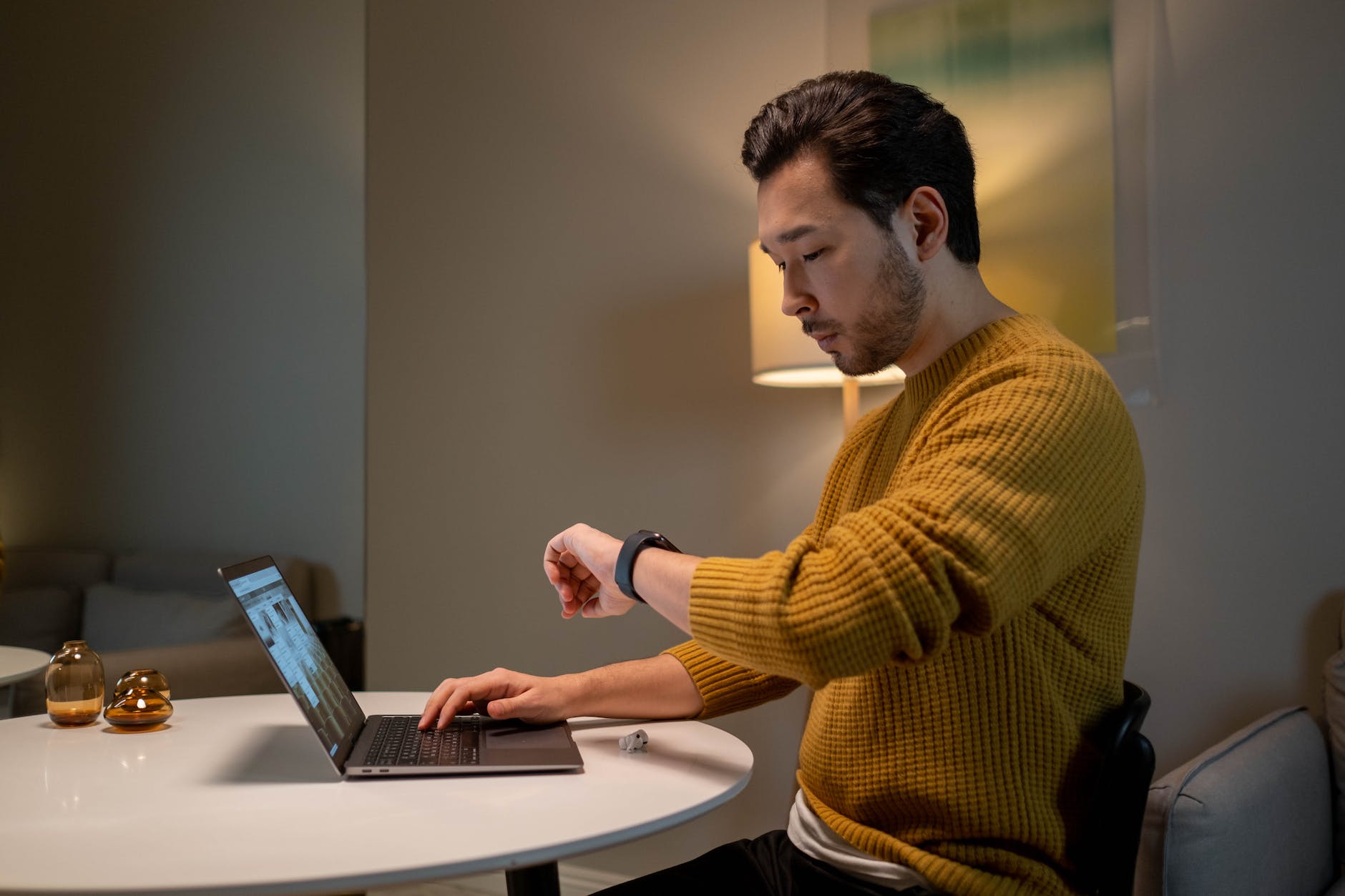 man in brown sweater looking at time on his smartwatch while using laptop